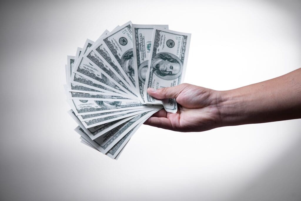 YouTube brand partnership deals: A hand holds 16 US $100 bills, fanned out over a white background. If our math is correct (and assuming we counted correctly) that's $1,600.